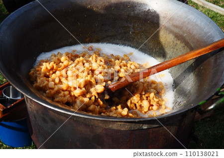 Stirring fat in a large vat on firewood. Pork rinds rendered, fried in fat, baked, roasted to produce pork cracklings or scratchings. Toasted brown cracklings. Large cast iron vat or cauldron. Stirring fat in a large vat on firewood. Pork rinds rendered, fried in fat, baked, roasted to produce pork cracklings or scratchings. Toasted brown cracklings. Large cast iron vat or cauldron. 110138021