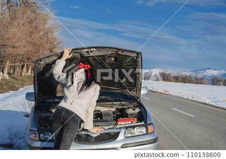 back of girl with sexy ass looks under hood at the engine of a broken car on road in winter 110138600