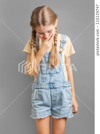 A little girl laughs covering her mouth with her hand 110139747