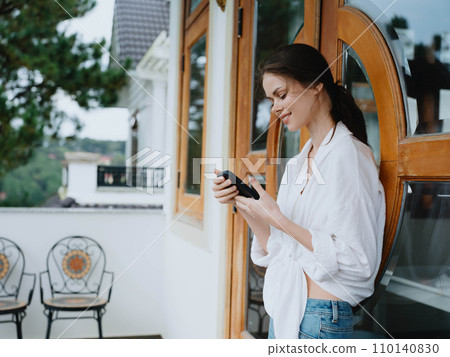 Woman on the balcony of the house with phone beautiful smile on a day off, beautiful view of nature in the mountains, lifestyle vacation in the hotel. Woman on the balcony of the house with phone beautiful smile on a day off, beautiful view of nature in the mountains, lifestyle vacation in the hotel. 110140830