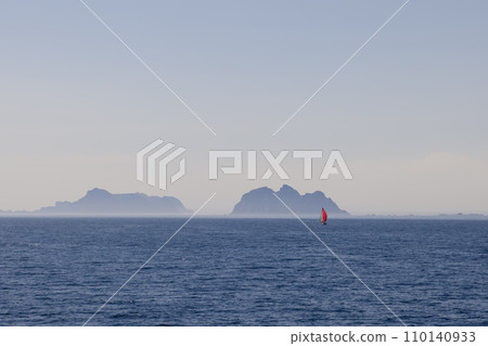 Solitary sailboat with red sail in calm North Sea, Lofoten backdrop 110140933