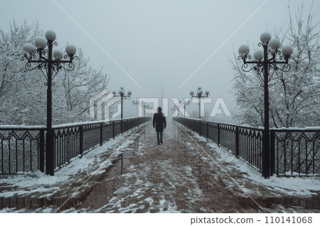 silhouette back man maniac walks on foggy bridge with lanterns in winter with snow and fog silhouette back man maniac walks on foggy bridge with lanterns in winter with snow and fog 110141068