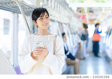 Young woman looking at a smartphone by train "Keio Electric Railway Co., Ltd." Young woman looking at a smartphone by train "Keio Electric Railway Co., Ltd." 110141104