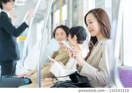 A young businesswoman commuting by train while looking at her smartphone. Photography cooperation: Keio Electric Railway Co., Ltd. A young businesswoman commuting by train while looking at her smartphone. Photography cooperation: Keio Electric Railway Co., Ltd. 110141519