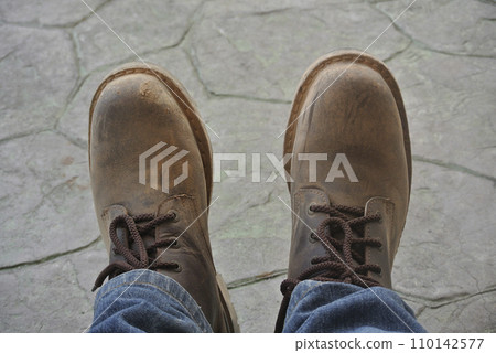 Top or side view of construction worker standing on construction site while wearing safety shoes. The shoes are dirty and dusty. Top or side view of construction worker standing on construction site while wearing safety shoes. The shoes are dirty and dusty. 110142577