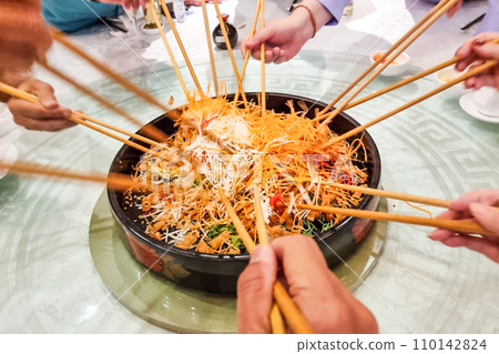 People mixing and tossing yusheng or yee sang during Chinese New Year dinner celebration. Slow shutter speed with motion blur intended. People mixing and tossing yusheng or yee sang during Chinese New Year dinner celebration. Slow shutter speed with motion blur intended. 110142824