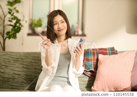 Middle-aged woman relaxing on the sofa and looking at her smartphone Middle-aged woman relaxing on the sofa and looking at her smartphone 110145538