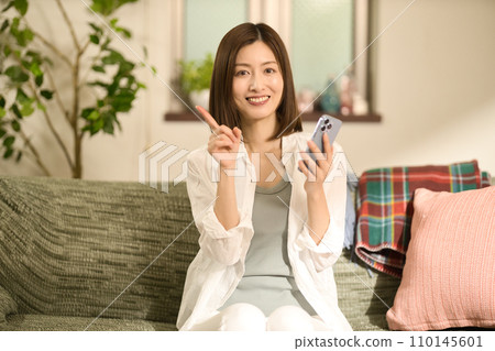 Middle-aged woman relaxing on the sofa and looking at her smartphone 110145601