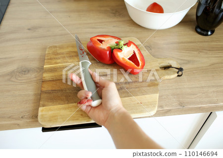 Woman cut her little finger with a knife while cooking vegetable salad on the kitchen. Female hand with blood holds knife with a sharp blade resulted in a cut and wounded finger cooking accident. 110146694