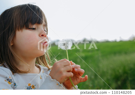 Child blowing a dandelion outside in a green field 110148205