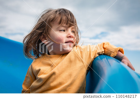 little girl in yellow clothes going down blue slide watching aside little girl in yellow clothes going down blue slide watching aside 110148217