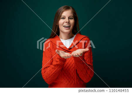 Positive young woman wearing a red sweater on a dark green background 110148455
