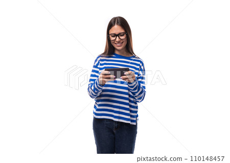 charming young slender caucasian woman with straight dark hair in a blue sweater uses a smartphone 110148457