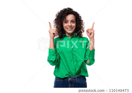 surprised young woman with black curly hair dressed in a green blouse points her fingers up 110148473