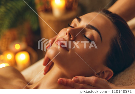 Woman enjoying massage in spa, lying on massage bed with closed eyes during facial massage treatment procedure. Woman enjoying massage in spa, lying on massage bed with closed eyes during facial massage treatment procedure. 110148571