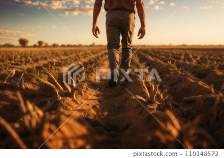 A farmer walking across a field of dry, cracked earth, a shovel over his shoulder, portraying the challenges faced by agriculture in arid regions 110148572