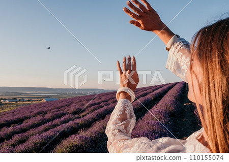 Woman lavender field. Happy carefree woman in a white dress walking in a lavender field and smelling a lavender bouquet on sunset. Ideal for warm and inspirational concepts in wanderlust and travel. Woman lavender field. Happy carefree woman in a white dress walking in a lavender field and smelling a lavender bouquet on sunset. Ideal for warm and inspirational concepts in wanderlust and travel. 110155074