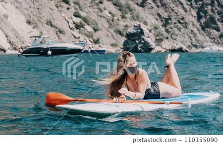 Woman sea sup. Close up portrait of happy young caucasian woman with long hair looking at camera and smiling. Cute woman portrait in bikini posing on sup board in the sea 110155090