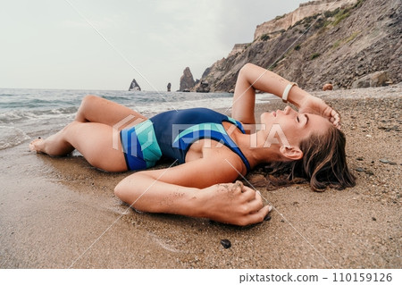 Woman summer travel sea. Happy tourist in blue bikini enjoy taking picture outdoors for memories. Woman traveler posing on the beach surrounded by volcanic mountains, sharing travel adventure journey Woman summer travel sea. Happy tourist in blue bikini enjoy taking picture outdoors for memories. Woman traveler posing on the beach surrounded by volcanic mountains, sharing travel adventure journey 110159126