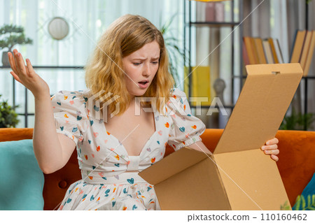 Angry dissatisfied shopper young woman unpacking parcel feeling upset, confused, wrong delivery Angry dissatisfied shopper young woman unpacking parcel feeling upset, confused, wrong delivery 110160462
