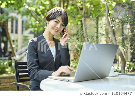 一名 30 多歲的女上班族在露台座位上打電話 110164477