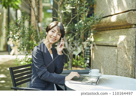 一名 30 多歲的女上班族在露台座位上打電話 110164497