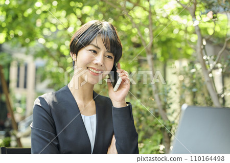 一名 30 多歲的女上班族在露台座位上打電話 110164498