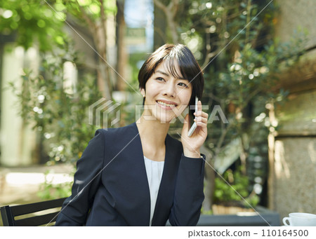 A female office worker in her 30s talking on the phone at a terrace seat A female office worker in her 30s talking on the phone at a terrace seat 110164500