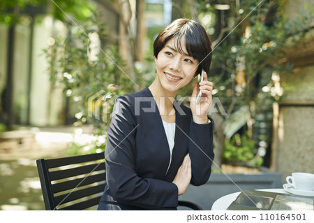 A female office worker in her 30s talking on the phone at a terrace seat A female office worker in her 30s talking on the phone at a terrace seat 110164501