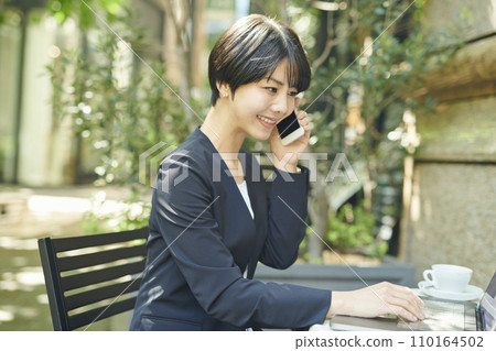 A female office worker in her 30s talking on the phone at a terrace seat A female office worker in her 30s talking on the phone at a terrace seat 110164502