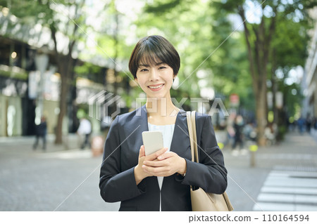 Female office worker in her 30s checking her smartphone in the city, smiling 110164594
