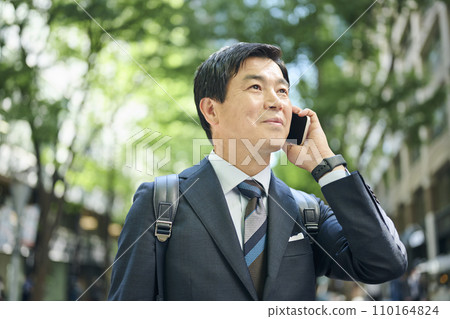 A 50s office worker walking around town while talking on the phone 110164824
