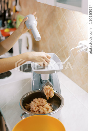 Housewife makes minced meat on an electric meat grinder pushing the meat in the tray with a pusher Housewife makes minced meat on an electric meat grinder pushing the meat in the tray with a pusher 110165954