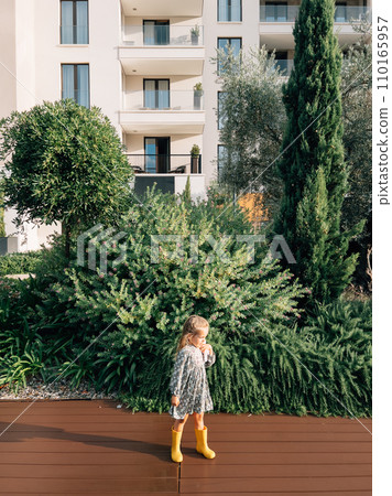Little girl stands on a wooden deck near a flowering juniper bush in the garden Little girl stands on a wooden deck near a flowering juniper bush in the garden 110165957