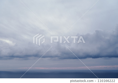 Dense storm clouds over the blue sea with a pink stripe of sunset Dense storm clouds over the blue sea with a pink stripe of sunset 110166222
