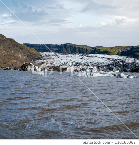 Solheimajokull picturesque glacier in southern Iceland. The tongue of this glacier slides from the volcano Katla. Beautiful glacial lake lagoon with blocks of ice and surrounding mountains. 110166362