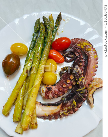 Fried octopus tentacles with asparagus and tomatoes lies on a plate Fried octopus tentacles with asparagus and tomatoes lies on a plate 110166472