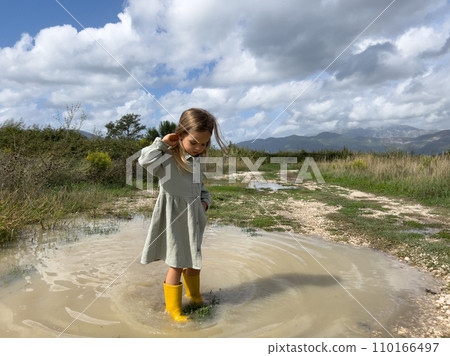 Little girl stands in a muddy puddle straightening her hair with her hand Little girl stands in a muddy puddle straightening her hair with her hand 110166497