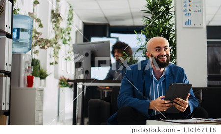 Employee comparing data on tablet while working in open space office. Unicorn business worker reviewing documents and annual statistics on device, trying to solve executive tasks. 110167118