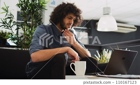 Creative employee looking to develop program in open floor plan office, working with past annual statistics to create new development strategy. Businessman thinks about startup growth. Creative employee looking to develop program in open floor plan office, working with past annual statistics to create new development strategy. Businessman thinks about startup growth. 110167123