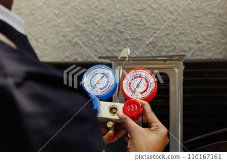 Pressure indicator tool able to find malfunctioning expansion valve and other issues, close up. Technician using manifold benchmarking gadget to read refrigerant levels of outdoor air conditioner Pressure indicator tool able to find malfunctioning expansion valve and other issues, close up. Technician using manifold benchmarking gadget to read refrigerant levels of outdoor air conditioner 110167161