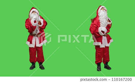 Saint nick cosplay does hush gesture to keep secret and maintain privacy over full body greenscreen backdorp. Young main character doing mute sign, asking for silence in studio. 110167200