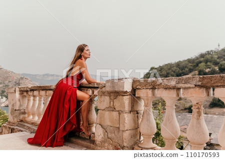 Woman travel portrait. Happy woman with long hair looking at camera and smiling. Close up portrait cute woman in a res long dress posing on backdrop of old travel city near sea Woman travel portrait. Happy woman with long hair looking at camera and smiling. Close up portrait cute woman in a res long dress posing on backdrop of old travel city near sea 110170593