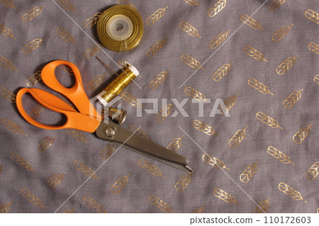 Spool of Metallic Gold Thread on Gray and Gold Chiffon Fabric 110172603