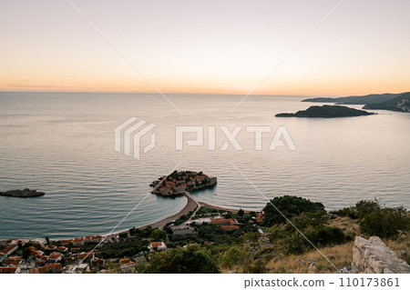 View from the mountain to the island of Sveti Stefan against the background of an orange sunset sky. Montenegro View from the mountain to the island of Sveti Stefan against the background of an orange sunset sky. Montenegro 110173861