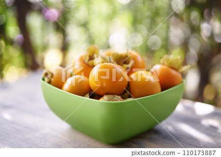 Full green bowl of ripe persimmons stands on a wooden table on the balcony Full green bowl of ripe persimmons stands on a wooden table on the balcony 110173887