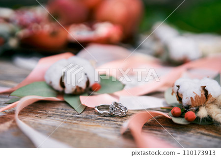 Wedding rings lie on a wooden table near ribbons and cotton flowers Wedding rings lie on a wooden table near ribbons and cotton flowers 110173913