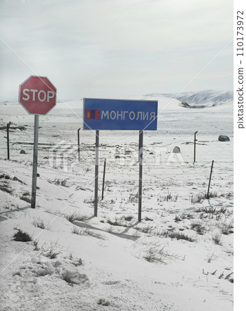 Sign marking the border crossing with Mongolia. Border is on a snowy mountain slope. Fence with barbed wire on the background winter snow slope. Sign marking the border crossing with Mongolia. Border is on a snowy mountain slope. Fence with barbed wire on the background winter snow slope. 110173972
