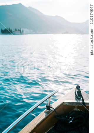 Bow of a wooden yacht sailing across the sparkling sea towards the mountains Bow of a wooden yacht sailing across the sparkling sea towards the mountains 110174047