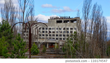 A dilapidated building with broken windows surrounded by overgrown trees. 110174547